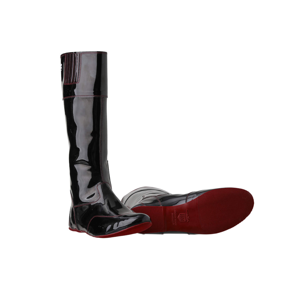 A pair of tall racing boots displayed against a white background. The boots are made of black material with burgundy exterior stitching and burgundy soles. They feature a back zip and a 1.5-2cm stretch feature around the calf. One boot is positioned sole down with the zipper done, while the other boot is laid down to showcase the sole of the boot.