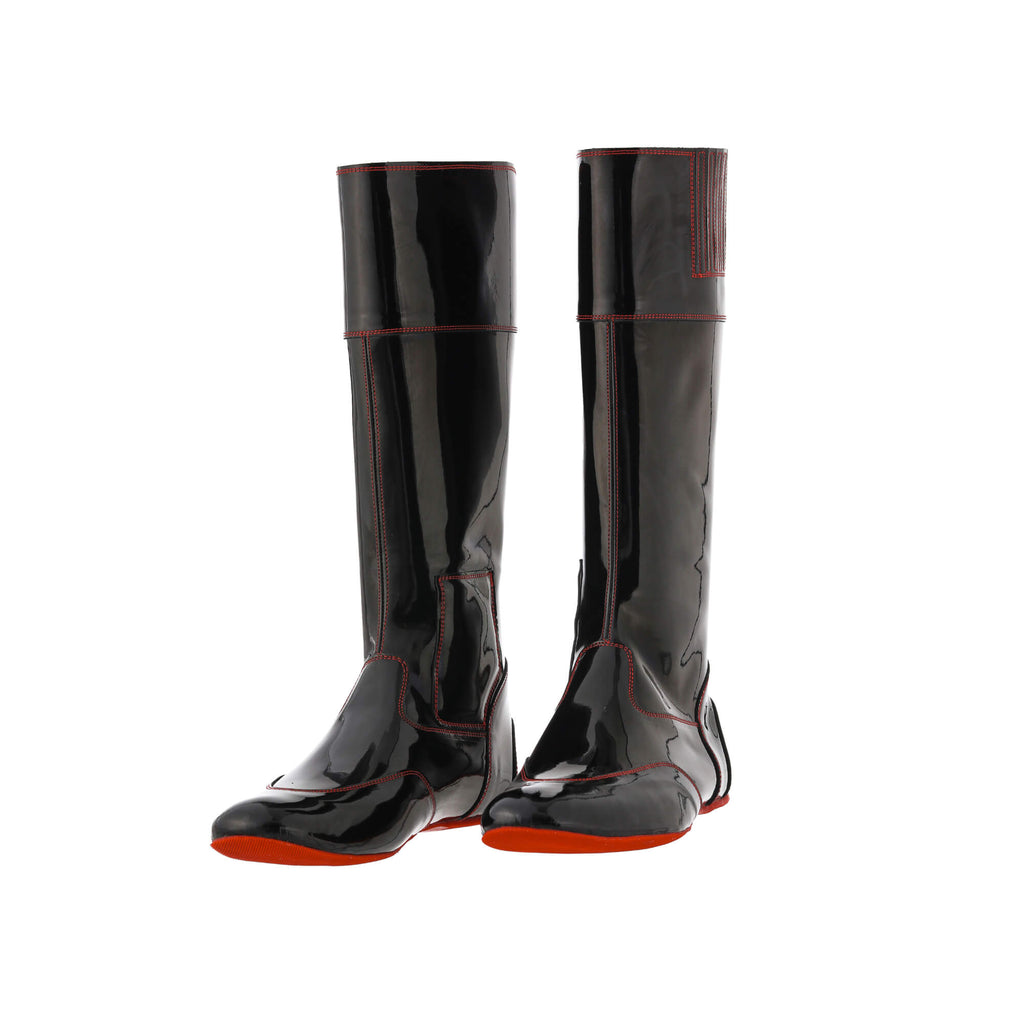 A pair of tall racing boots displayed against a white background. The boots are made of black material with red exterior stitching and red soles. They feature a back zip and a 1.5-2cm stretch feature around the calf. Both shoes are positioned sole down with the zipper done, angled slightly to one side.