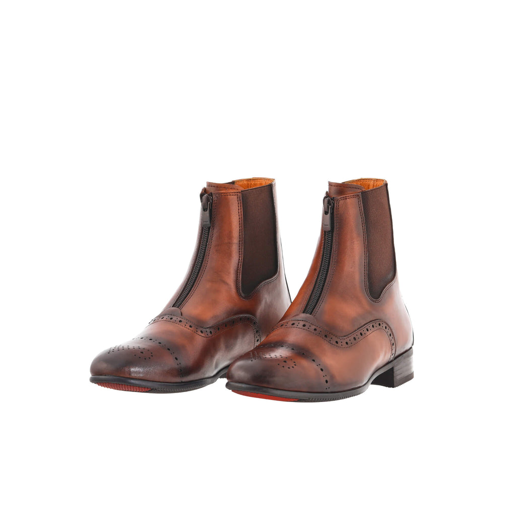 A pair of brown patina leather wingtip style boots displayed against a white background. Both boots are positioned sole-down with the front zip closure done. The angle of the display is slightly positioned to one side, offering a dynamic perspective.