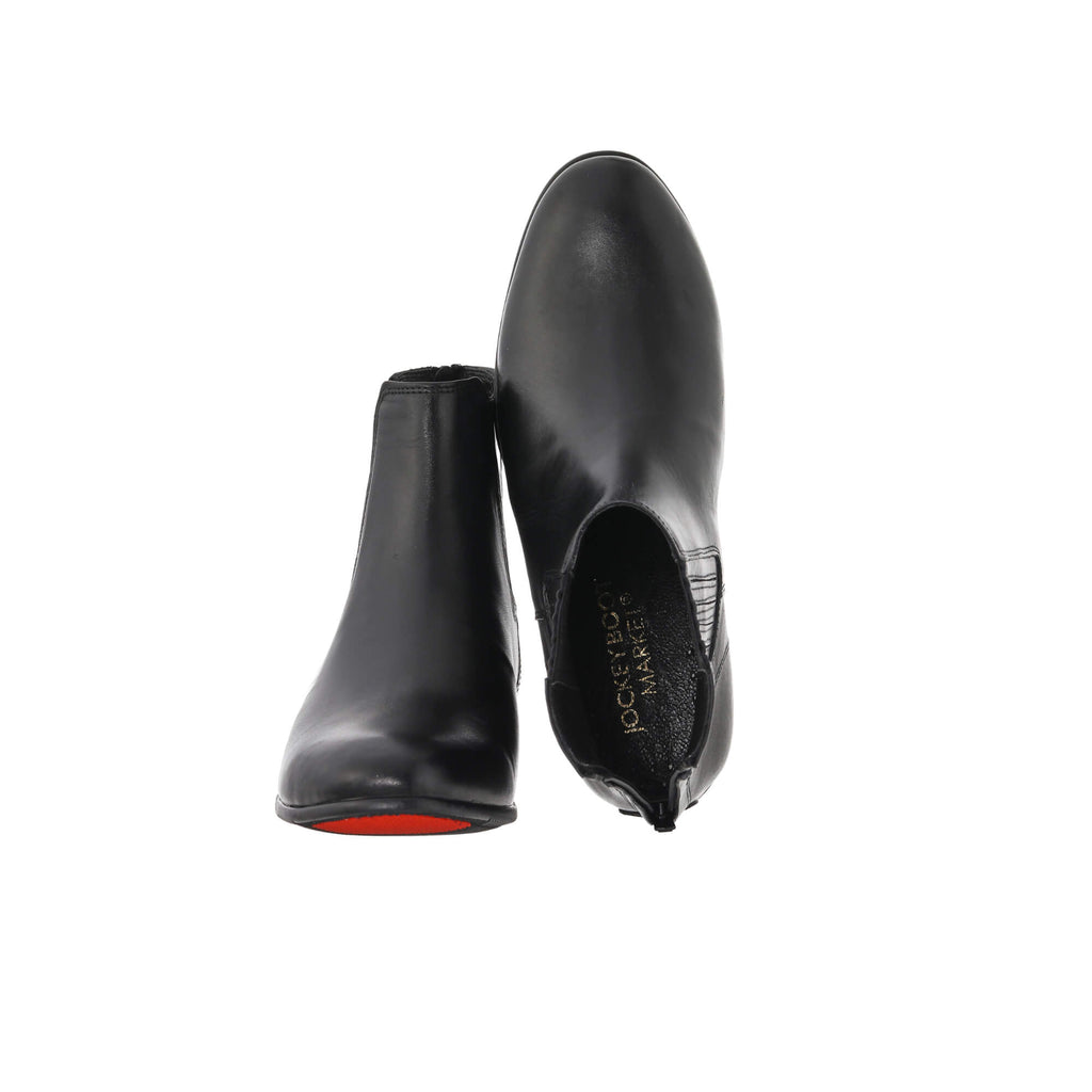 A pair of short classic black leather boots with a back zip, set against a white background. The first shoe's sole is resting on the floor, with the zip secured. The second shoe is displayed upside down, revealing the sole, with the zip undone to showcase the interior design.