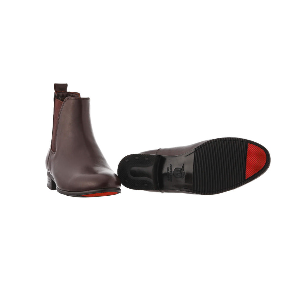 A pair of classic brown leather boots with an easy slide-in design, presented on a white background. One shoe is displayed sole down, while the other shoe is laid down to highlight the sole, which features a red tip as their signature design element.