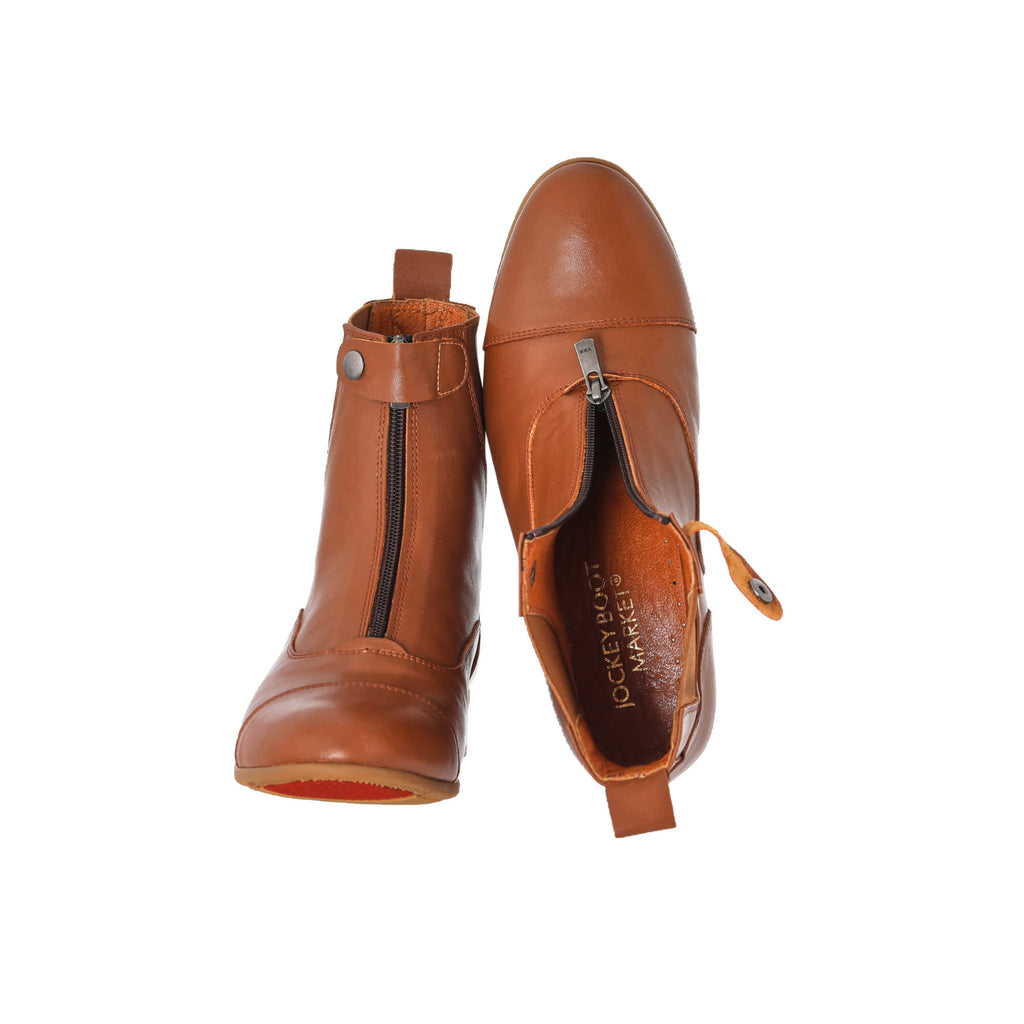 A pair of tan leather short boots with a front zip and buckle, showcased on a white background. The first shoe's sole is placed on the floor with the buckle and zip done, while the second shoe, upside down, displays the inside of the shoe with the undone buckle and front zip.