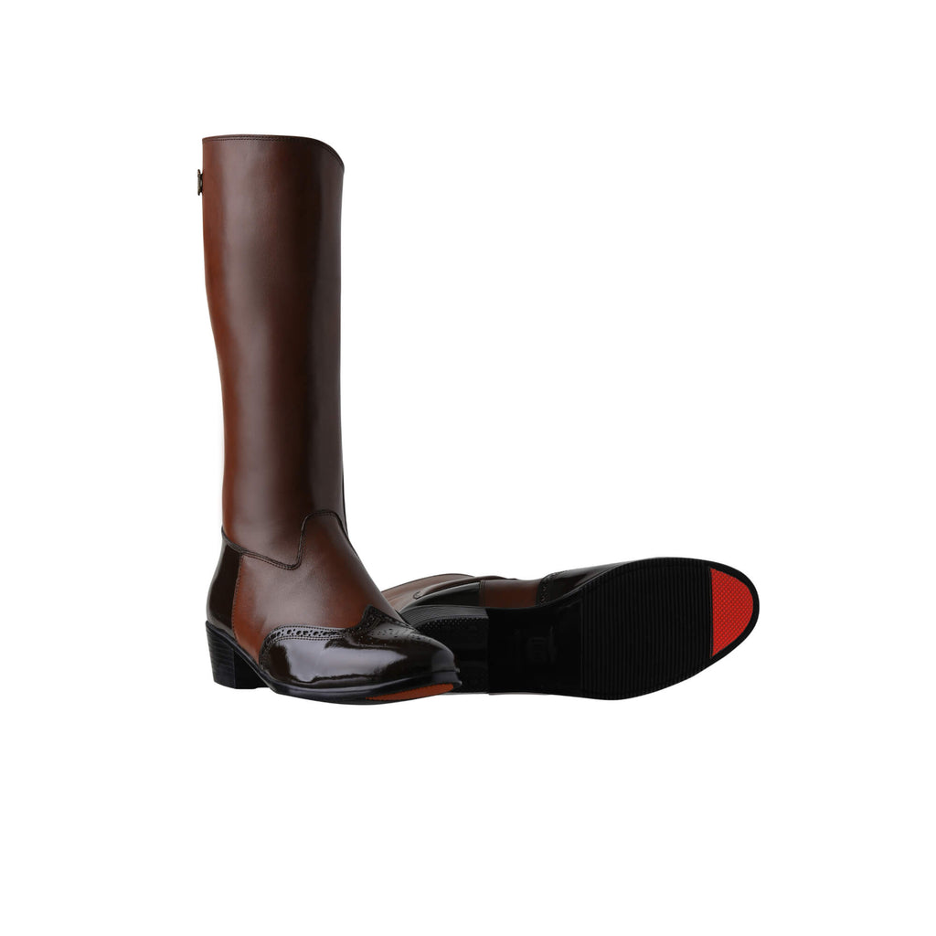 A pair of tall brown leather Cuban heel boots with brown wingtip accents. The boots feature a back zip and are displayed against a white background. One boot is positioned sole down with the zipper done, while the other boot is laid down to showcase the sole, featuring a red tip design.